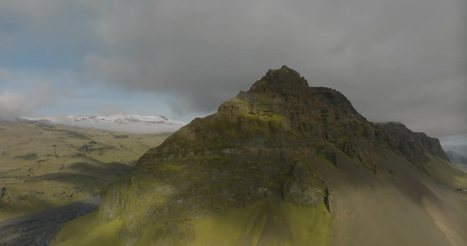 A dramatic aerial shot slowly reveals a stunning, moss-covered mountain in Iceland as clouds cast moving shadows over the rugged landscape