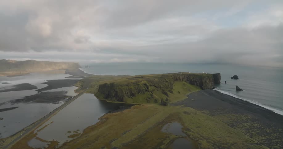 A stunning aerial view of the dramatic green cliffs and black sand beach of Dyrhólaey on the southern coast of Iceland