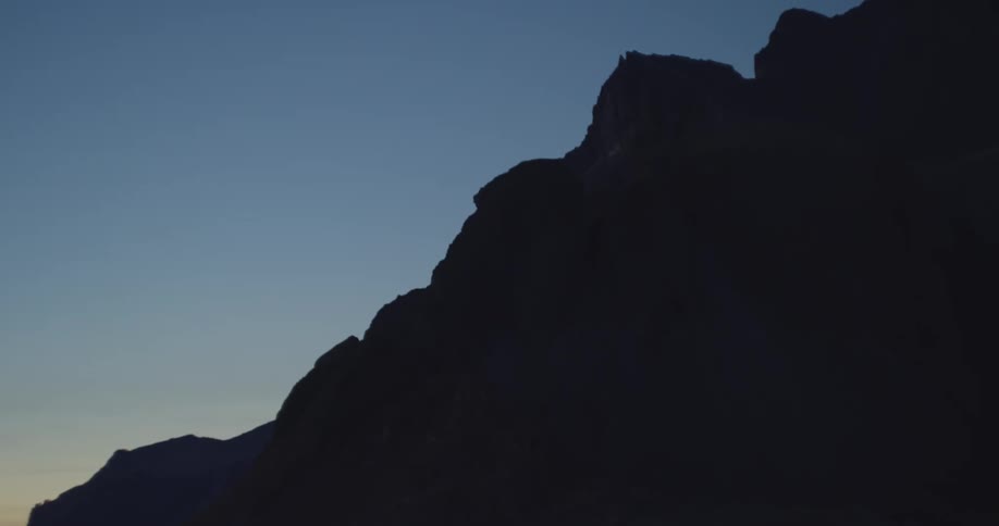 The dark silhouette of a rugged mountain stands stark against a clear, deep blue twilight sky