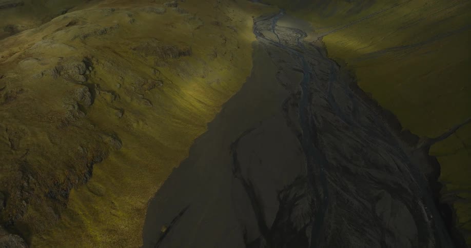 Epic aerial reveal of a vast volcanic river valley cutting through moss-covered mountains in the Icelandic highlands
