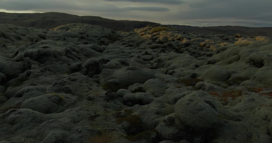 The sun sets over a vast and surreal landscape of moss-covered volcanic rock formations
