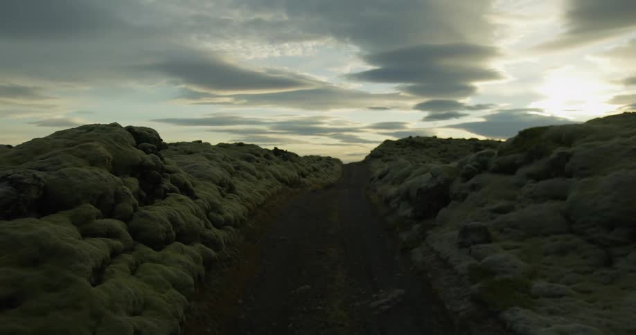 A slow journey down a secluded dirt path cutting through an otherworldly moss-covered lava field in Iceland at dusk