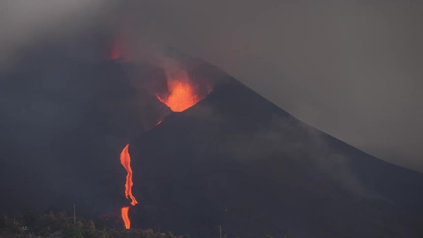 A volcano erupts with fiery lava flowing down its dark slopes amidst thick plumes of smoke and ash