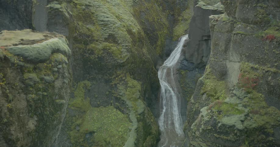 A stunning waterfall winds its way down through a deep, ancient canyon covered in vibrant green moss