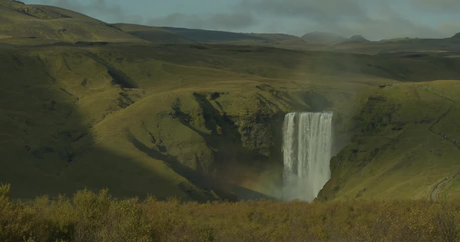 A slow reveal of the majestic Skógafoss waterfall cascading down a cliff in the vast, green Icelandic highlands