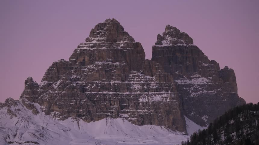Epic timelapse of a golden sunset fading to a purple dusk over the snowy Tre Cime di Lavaredo mountains in the Dolomites