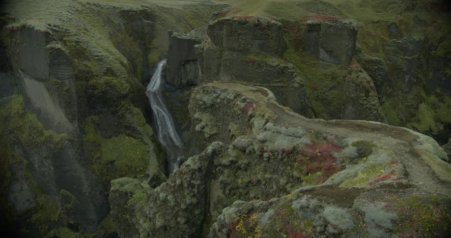 A slow reveal of a breathtaking waterfall cascading through the deep, moss-covered Fjadrargljufur canyon in Iceland