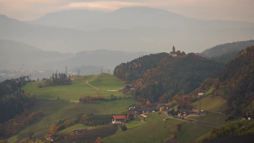 A tranquil time-lapse of sunlight moving across a picturesque autumn valley with a church perched on a hill
