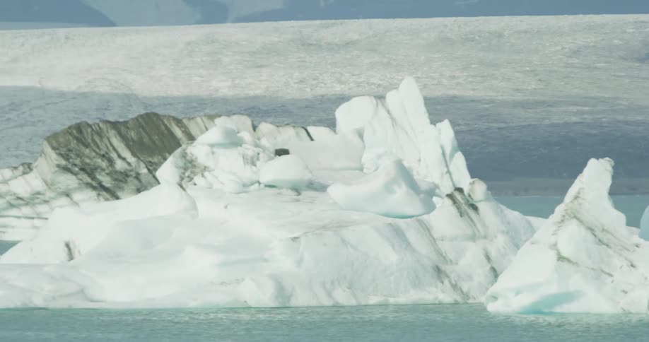 A slow pan across majestic icebergs floating in a vast glacial lagoon in an arctic landscape