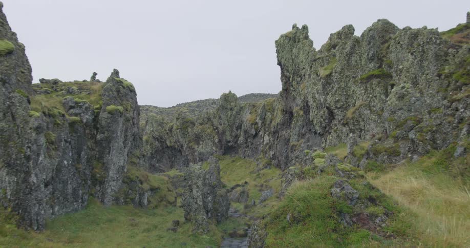 A wide, slow zoom-out reveals a rugged, moss-covered volcanic landscape on an overcast day