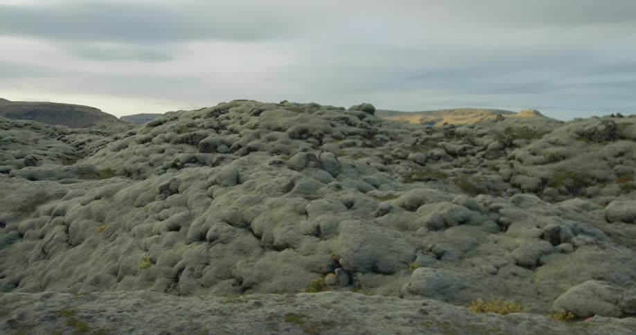 A slow tracking shot across a vast, otherworldly lava field covered in thick, green moss under a cloudy Icelandic sky
