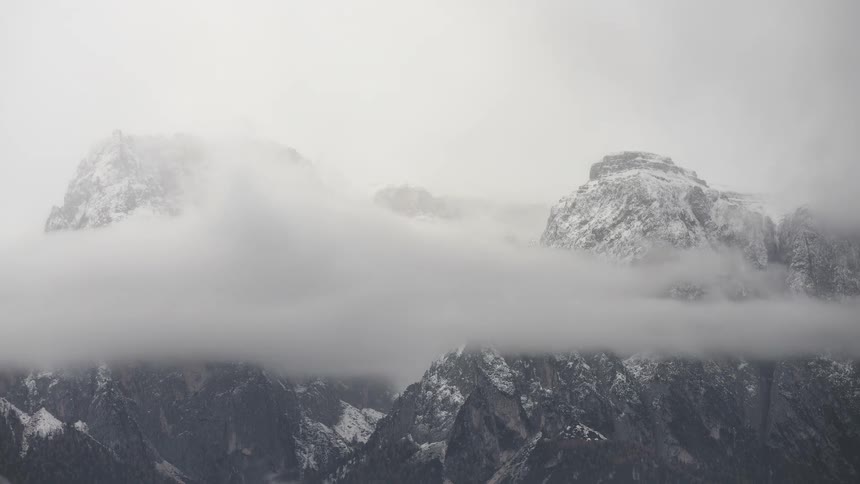 A serene timelapse captures clouds and fog rolling over the majestic, snow-covered peaks of a rugged mountain range