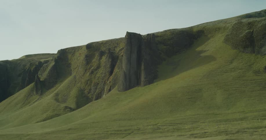 A tracking shot reveals a vast green landscape with unique rock formations jutting from the hillsides