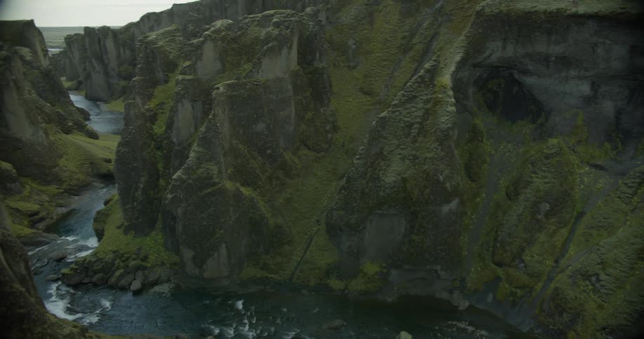 A slow pan reveals a magnificent waterfall and a flowing river winding through the deep, moss-covered Fjadrargljufur Canyon in Iceland