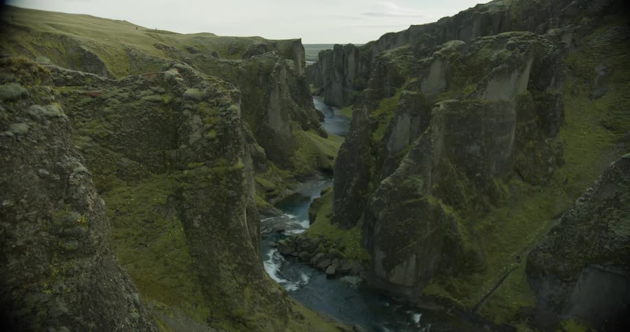 A slow tilt up reveals a breathtaking view of a majestic moss-covered canyon with a river flowing through it in Iceland