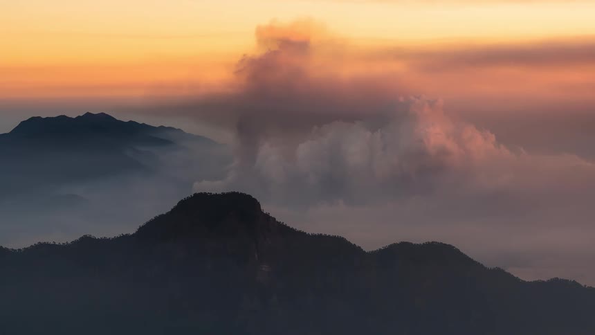 A serene timelapse of clouds and fog rolling over a majestic mountain range during a golden sunset