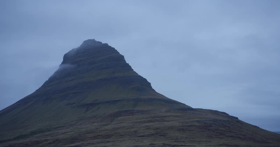 Clouds drift over the peak of Kirkjufell mountain on an overcast day in Iceland