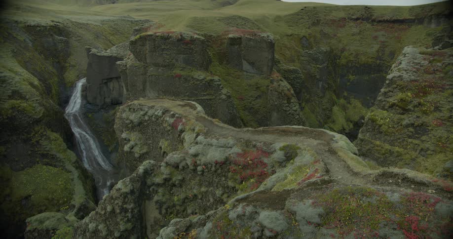 A picturesque view of Iceland's Fjaðrárgljúfur canyon, where a narrow path winds along mossy cliffs above a cascading waterfall