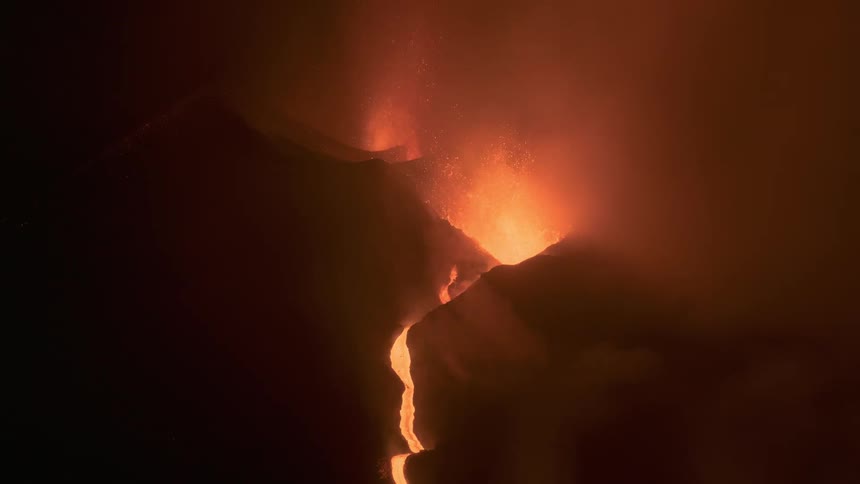 A powerful volcanic eruption at night sends streams of molten lava flowing down the mountainside amid thick, glowing smoke