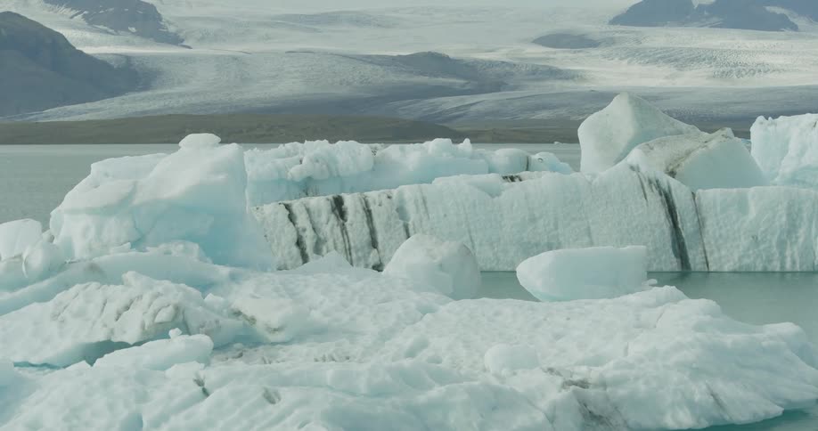 Majestic icebergs float serenely in a glacial lagoon with a vast, distant glacier stretching across the horizon