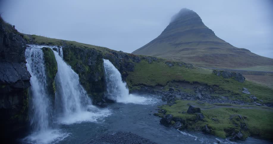 The iconic Kirkjufell mountain stands majestically behind the cascading Kirkjufellsfoss waterfall on a cloudy day in Iceland
