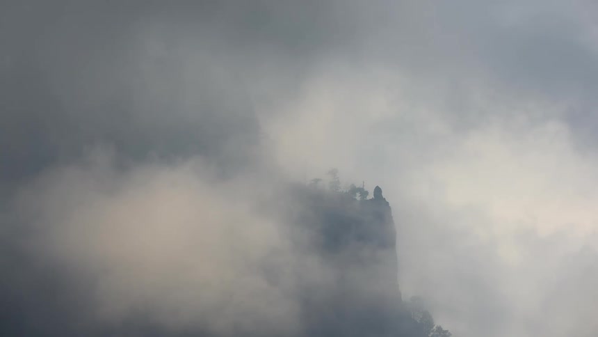 Mysterious clouds and fog slowly reveal a remote mountain peak dotted with trees
