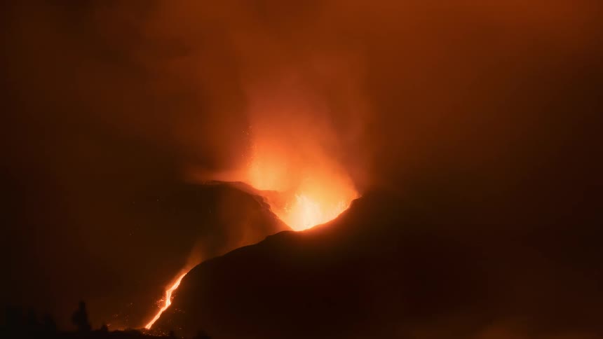 A fiery volcano erupts at night, with molten lava flowing down the mountain slope and thick smoke filling the air