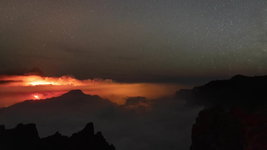 Dramatic night time-lapse captures a volcanic eruption with lightning and the moon setting to reveal the starry Milky Way over misty mountains