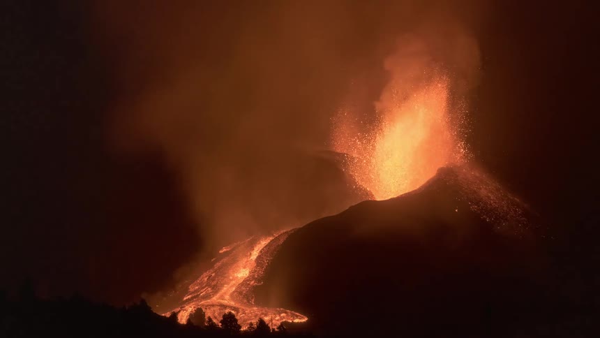 A powerful volcanic eruption illuminates the night sky as fiery lava explodes from the crater and flows down the mountainside