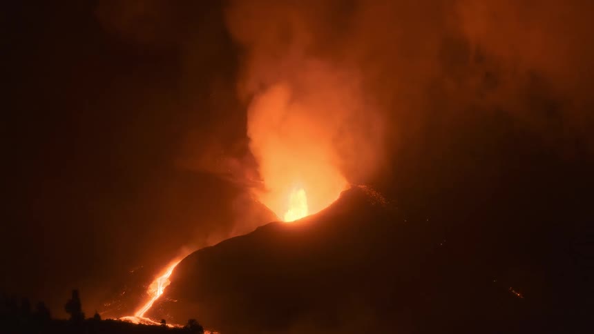 Dramatic nighttime view of a volcanic eruption with a river of lava flowing down its slope amidst thick smoke