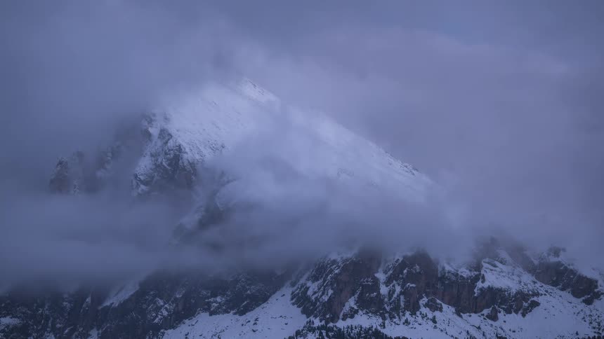 A time-lapse of heavy clouds slowly parting to reveal the majestic peak of a snow-covered mountain