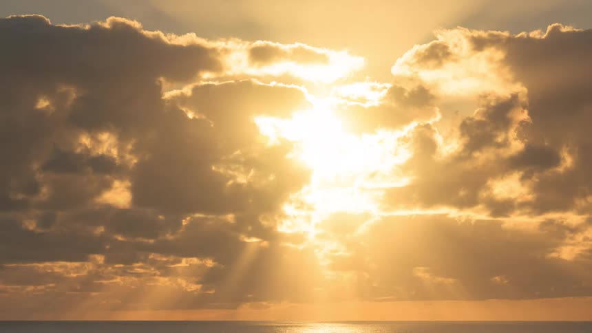 A dramatic timelapse captures clouds parting over the ocean to reveal a glorious golden sunrise with brilliant sun rays