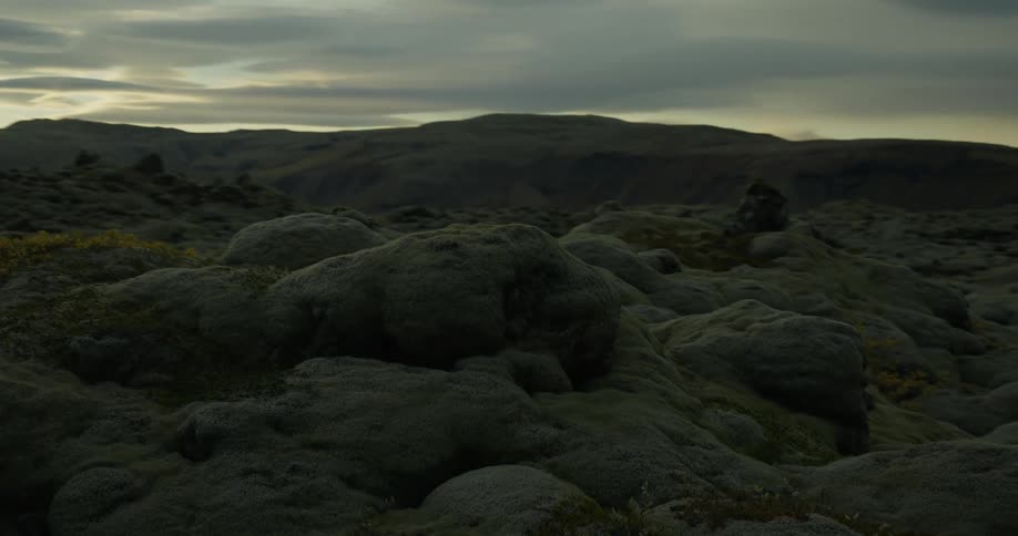 A slow pan reveals an expansive, moss-covered volcanic landscape under a dramatic, cloudy sky at dusk
