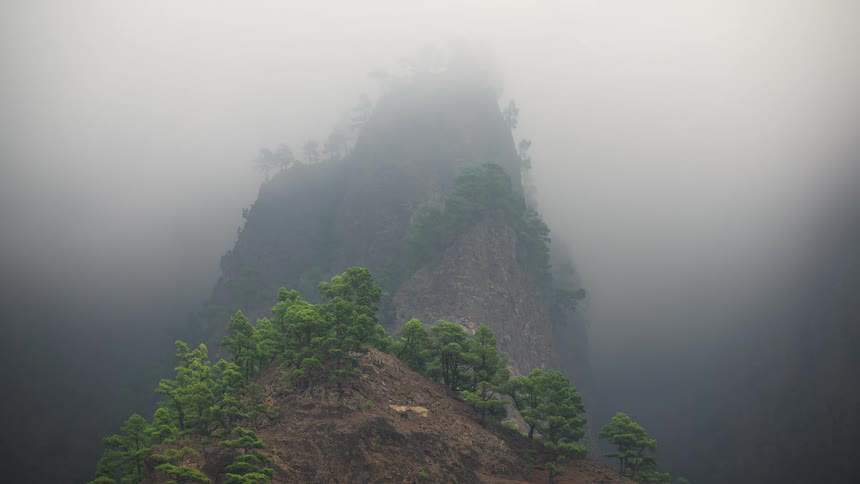A time-lapse of dense fog rolling over a beautiful green mountain peak