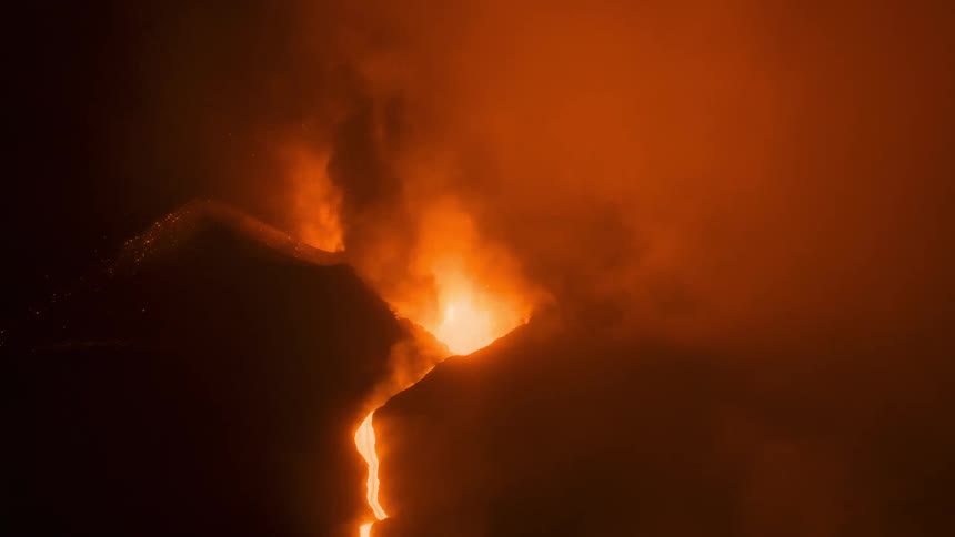 Fiery lava erupts from a volcano at night, with molten rock flowing down the mountain slope amidst thick smoke