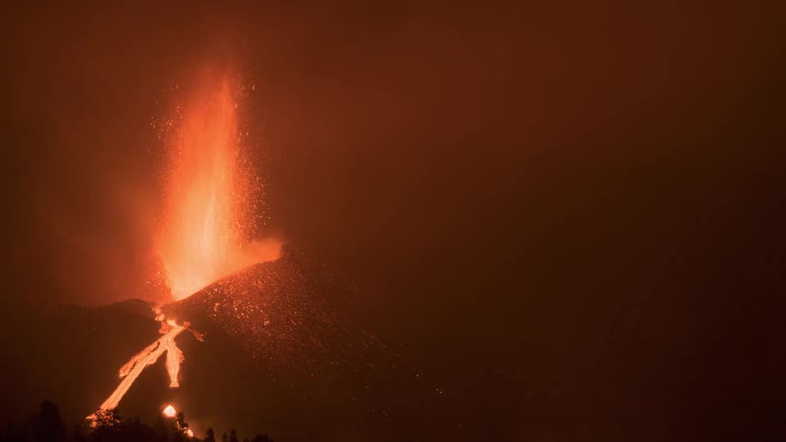 A volcano erupts with fiery lava spewing into the smoky night sky