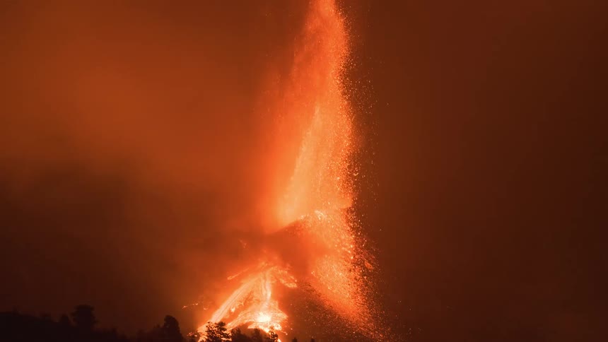 A volcano violently erupts at night, shooting a fountain of lava and ash into the thick, smoke-filled air