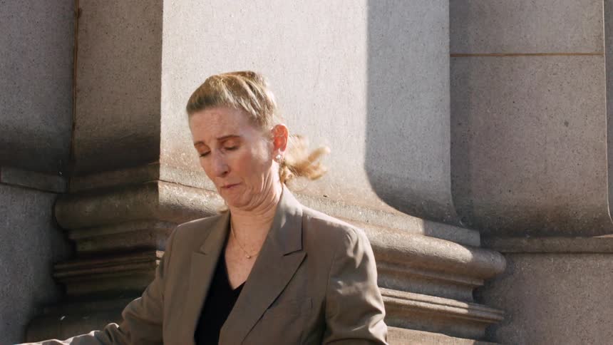 Slow motion footage of a businesswoman grooving by a stone pillar as a frisbee unexpectedly flies by