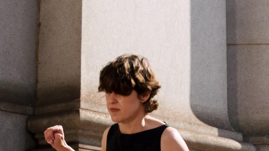 A dramatic slow-motion close-up shows an emotional woman in a black dress looking up towards the light