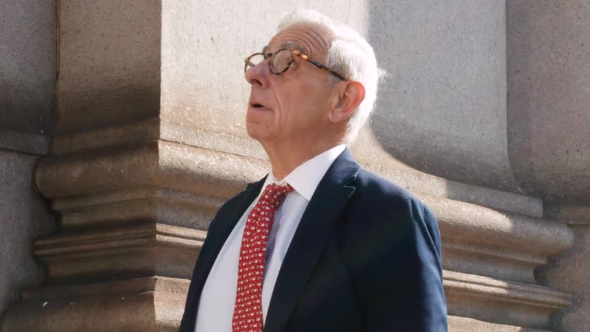 A distinguished elderly businessman in a suit and tie looks up in shocked amazement in slow motion