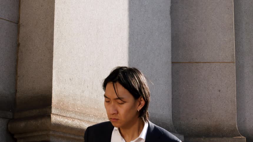 Slow motion medium shot of a Japanese businessman in a suit, tilting his head back to feel the warmth of the sun on his face