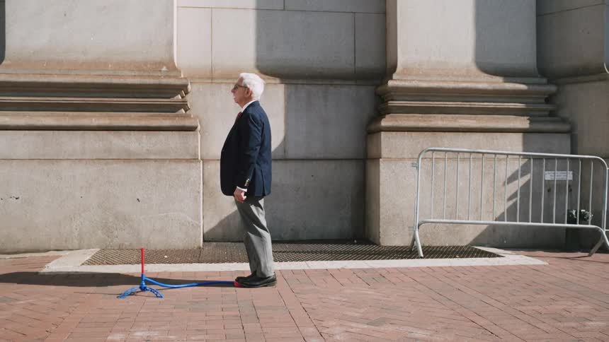 A senior man dressed in a blazer launches a toy rocket on a city sidewalk in slow motion