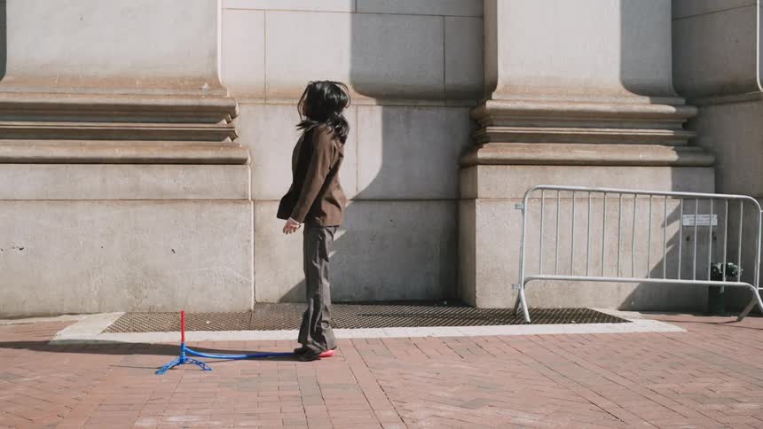A woman in a brown blazer jumps on a toy rocket launcher, sending it soaring into the air in slow motion