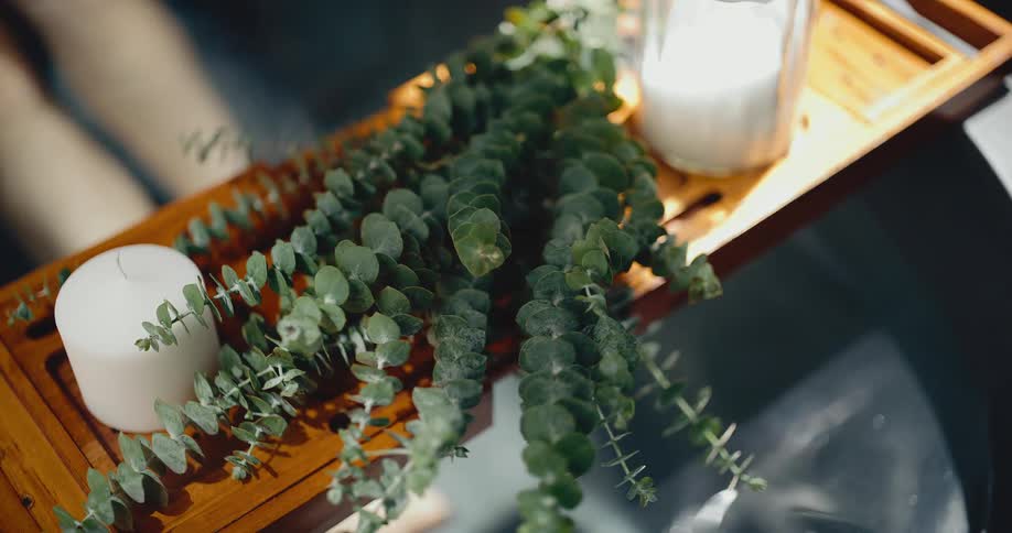 Eucalyptus branches and candles rest on a wooden tray, creating a spa-like atmosphere in a steamy bath