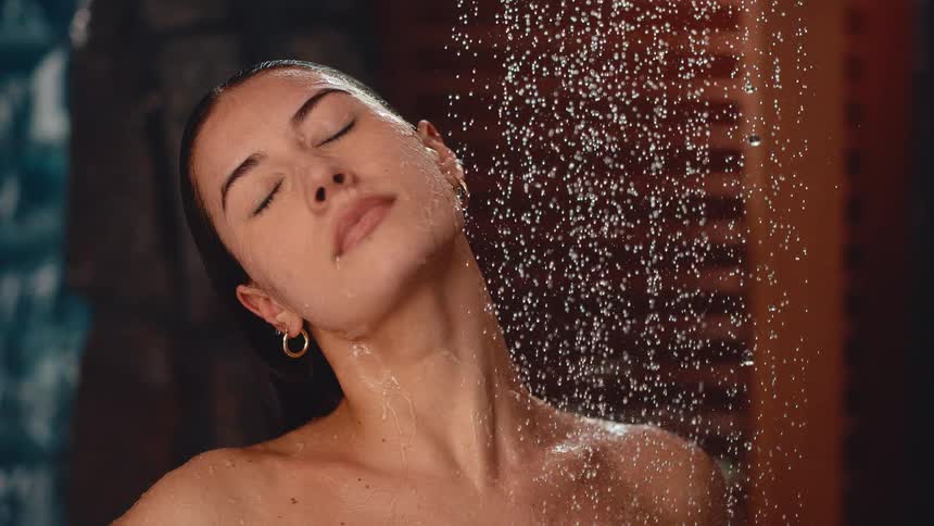 A serene woman enjoys a refreshing shower with her eyes closed in a slow-motion cinemagraph