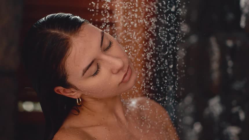 Slow motion cinemagraph of a beautiful young woman enjoying a refreshing and relaxing shower with her eyes closed