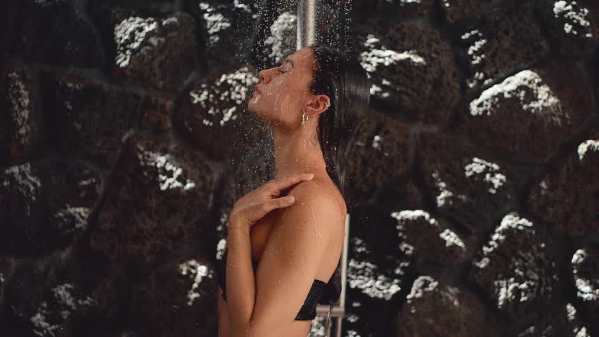 Cinemagraph of a serene woman enjoying a refreshing shower in slow motion against a dark stone wall