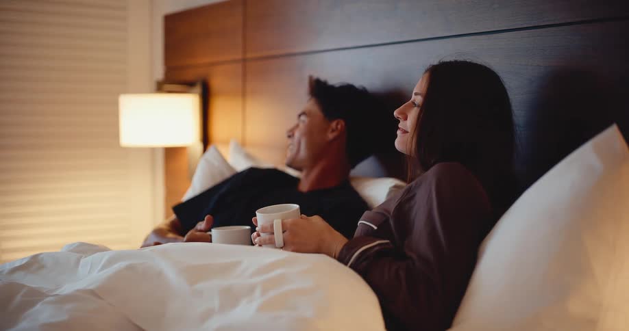 A young happy couple talks and relaxes in bed with their morning coffee