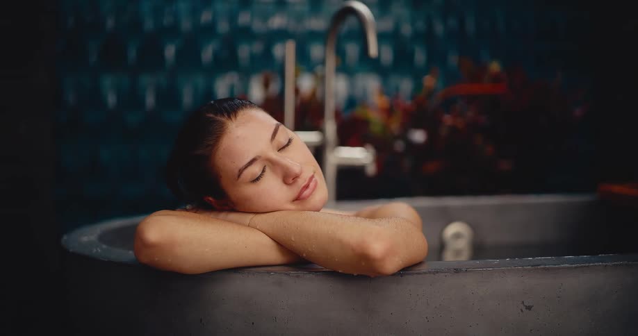 An attractive woman relaxes in a modern stone bathtub, closing her eyes in a moment of peaceful self-care