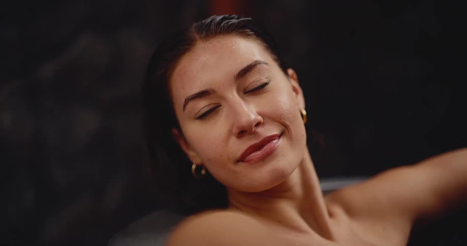 A beautiful, smiling woman with wet hair peacefully relaxes in a steamy spa
